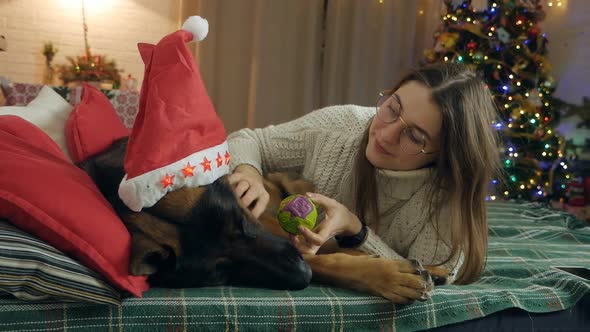 A Beautiful Girl Lies on the Sofa with Her Dog German Shepherd Against the Backdrop of Christmas