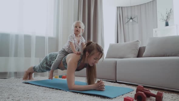 Mother and the Little Baby are Engaged in Yoga in Sportswear at Home alt