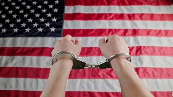 Caucasian Hands Shackled in Silver Handcuffs Against the USA Flag