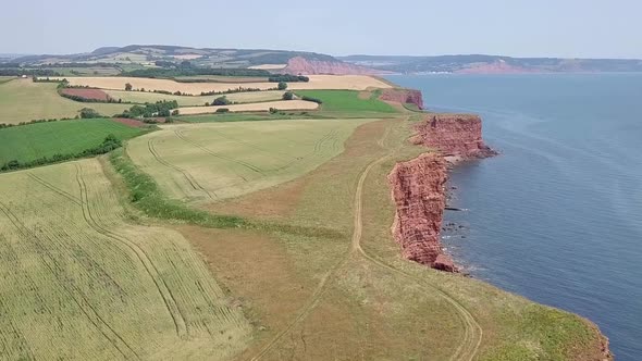 STATIC CROP, Slow pan across green seaside fields by red sandstone cliffs alt