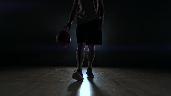 Basketball Player in Sportswear Red Shorts and a Blue T-shirt Goes on a Dark Basketball Court in the alt