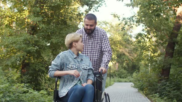 Hipster Man Rolls Caucasian Disabled Woman in Wheelchair and Talks to Her alt
