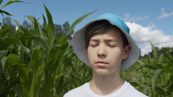 Portrait of a Serious Sleepy Boy in a Hat Standing in a Corn Field and Looking at the Camera