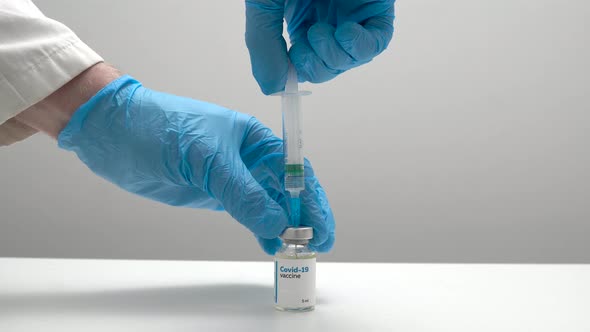 Close up of a doctor in medical blue gloves filling a syringe with a dose of coronavirus vaccine