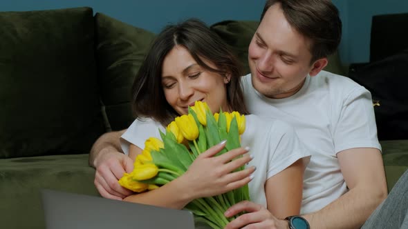 Woman That Is Working at the Computer Receiving a Bouquet of Yellow Tulips From Her Husband alt
