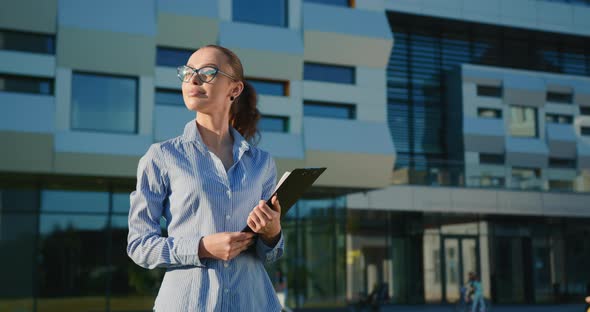 A Businesswoman is Walking with a Folder of Documents Near the Business Center alt