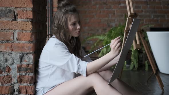 Artist Paints a Picture in a Home Studio in the Style of a Loft. Portrait of an Attractive Girl alt