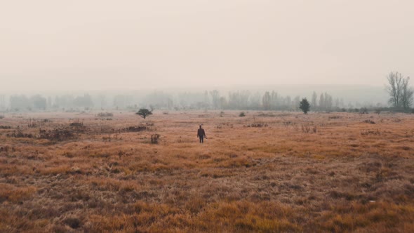 A documentarist with a camera walking in a brown misty autumn field. alt