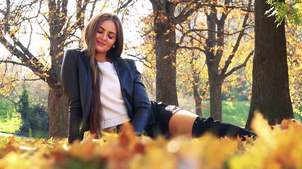 Young Beautiful Woman Lies on the Foliage in Autumn Park and Smiles To Camera alt