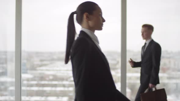 Businesspeople Walking in front of Panoramic Window in Office Building alt