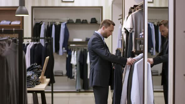 A Side View Slow Motion Shooting of a Man in a Clothing Boutique Standing Near the Clothes Hanger
