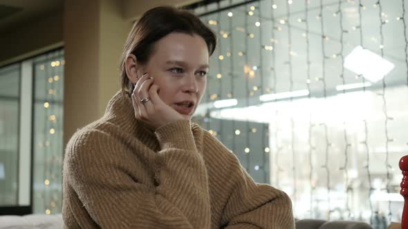 a Woman in a Beige Sweater Sits in a Restaurant and Talks to Someone