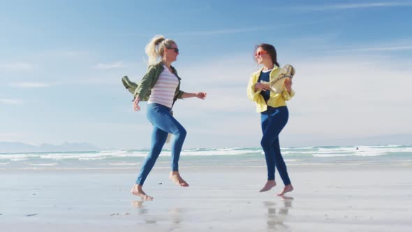 Happy two caucasian female friends having fun, walking along beach alt