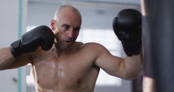 Caucasian male trainer wearing boxing gloves training with punching bag at the gym alt