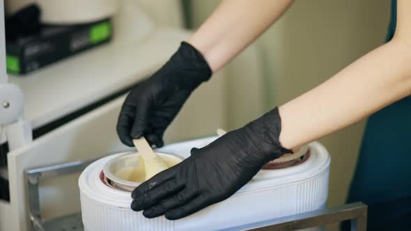 Master of Hair Removal Prepares Wax for Depilation Using Wooden Spatula alt