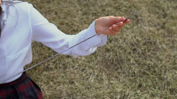 Girl Sits on Grass and Gently Strokes Blade of Katana. Beauty Looks with Proud alt