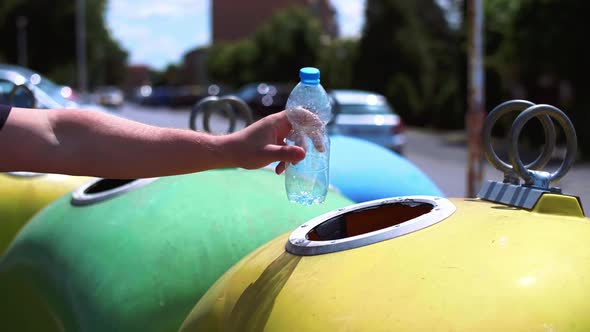 Man’s hand throwing plastic, empty bottle into recycling bin alt