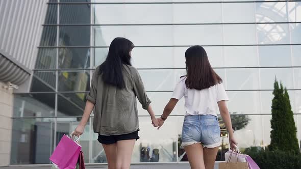 Asian Female Best Friends with Many Bags in Their Hands Walking Near Shopping Mall Holding alt