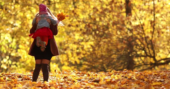 Pretty Little Girl in Black Jacket Smiles and Rejoices in the Autumn Park with Her Happy Mum