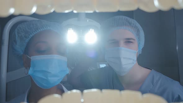 View From Open Patient Mouth of Dentist and Assistant Adjusting Lamp and Examining Teeth alt