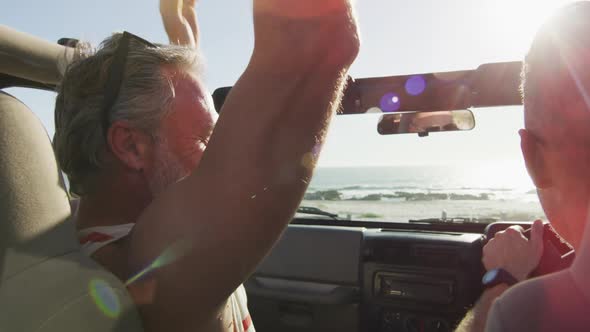 Happy caucasian gay male couple sitting in car and high fiving on sunny day at the beach alt