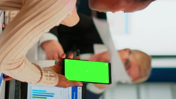 Black Businesswoman Sitting at Conference Desk Holding Smartphone with Green Screen alt