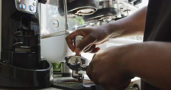 Close up of african american male barista making coffee using coffe machine at cafe alt