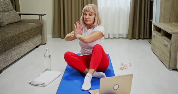 Elderly Woman Following an Online Yoga Class Working Out at Home on a Laptop Computer in a Health alt