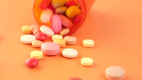 Close Up of Many Colorful Pills and Capsules Spilling on Orange Background alt