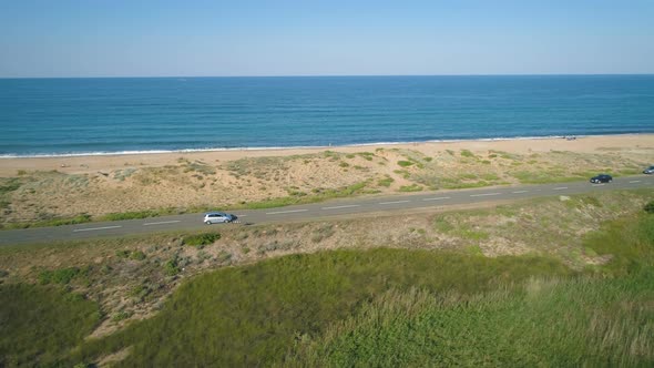 Cars Driving Along a Straight Coastal Road with Beautiful Sea Horizon in Sunny Day alt