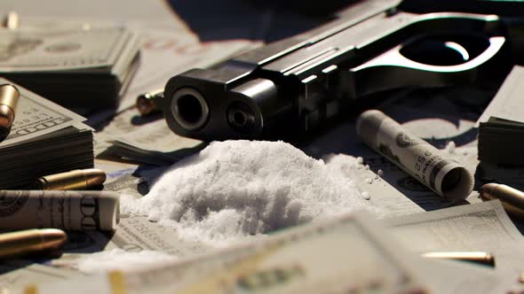 Ammo bullets and a gun on a table covered with countless dollar bills and drugs alt
