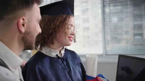 Distance Education Joyful Woman in Academic Dress with a Male Friend Receiving Her Diploma Online alt