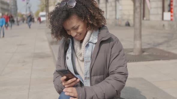 Beautiful Girl with Afro Haircut Sitting on Bench at City Street alt