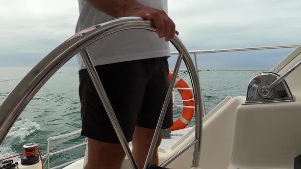 Midsection of a captain steering a sailing boat on an overcast day. alt