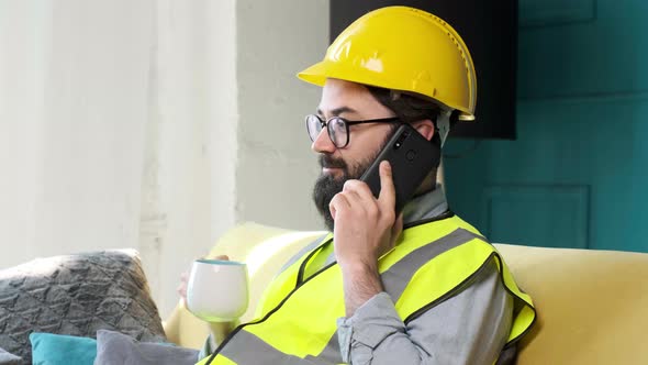 Architect Talking on the Phone and Drinking a Cup of Tea Relaxing on Sofa alt