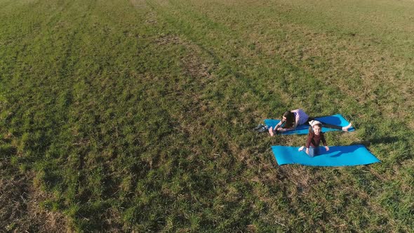 Mom with Her Little Daughter Stretching on the Mat on the Field in Warm Summer Day. Aerial Panoramic