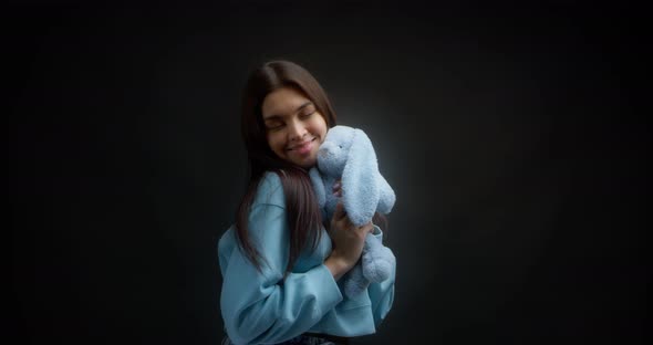 Cute Brunette with Long Hair in a Blue Jumper Hugs a Soft Toy Bunny