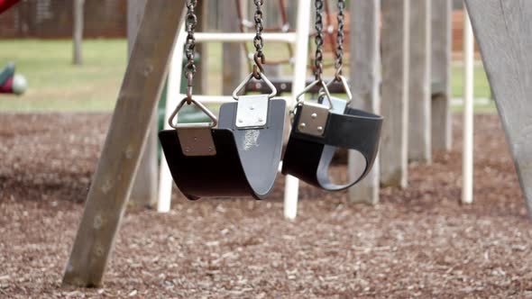Empty swing set in an empty playground. Swings blowing in the wind. alt