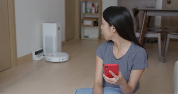 Woman Use of Mobile Phone to Control Robotic Vacuum Cleaner at Home alt