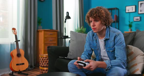 Teenager Boy Playing Game with Joystick Enjoying Sitting on Sofa in Living Room at Home alt