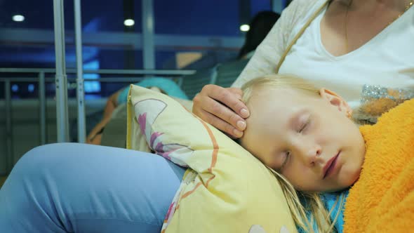 A Woman is Stroking a Girl Sleeping on Her Lap Sitting in the Terminal of the Airport alt