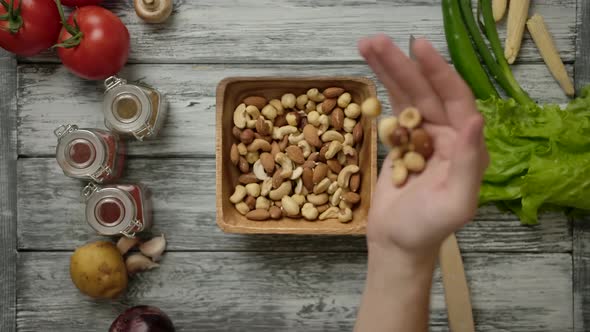 Hand Pours Nuts Into a Wooden Bowl on the Kitchen Table alt