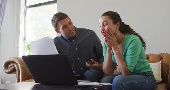 A young caucasian couple talking and paying their bills using a laptop alt