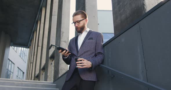 Office Manager in Business Clothes which Using His Mobile on the Steps of Business Center alt