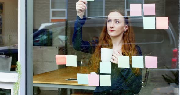 Business executive reading at sticky note while having cup of coffee alt