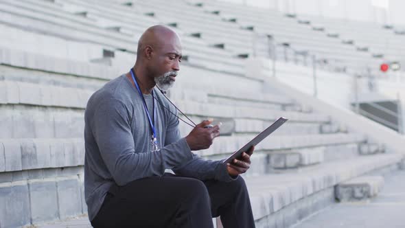 African american male coach sitting, time checking and making notes alt
