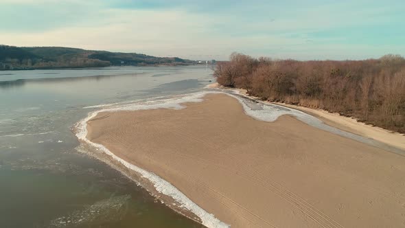 Aerial Drone Footage of Flight Over a Sandy Shore with a Small River in Winter