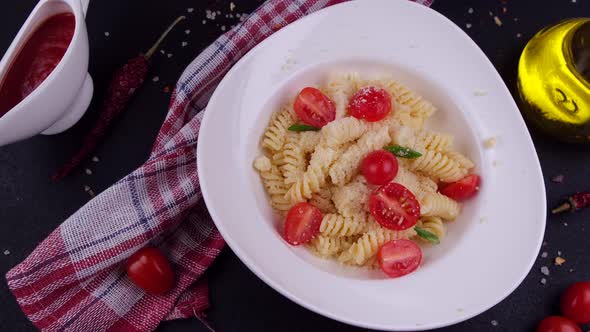 Rotating Plate with Fuzulli Pasta From Above Falling Parmesan Cheese with Cherry Tomatoes on a Black