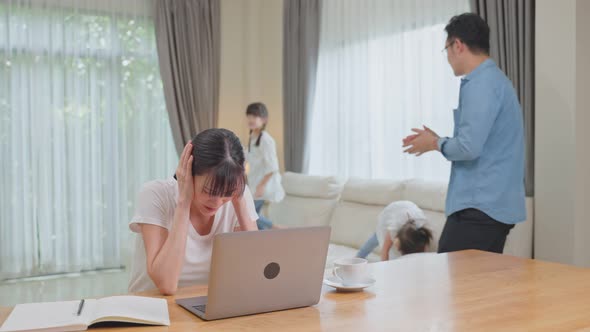 Asian mother work using computer at home with young children and husband play aroung the house. alt