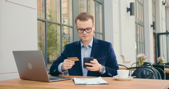 A Businessman Is Sitting at a Table in a Cafe and Working alt